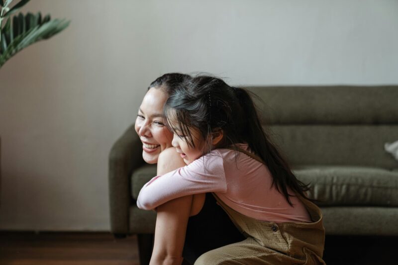 A child hugging her smiling mother from behind
