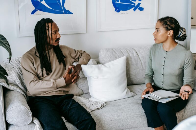 A man sitting on a couch with a therapist, who is speaking a taking notes