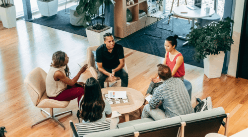 a group of five sit around a table in an office.